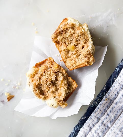 Overhead close-up of a cinnamon apple muffin cut in half, showing the moist, fluffy crumb, soft chunks of apple and streusel topping, on a white marble background.