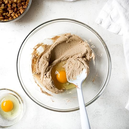 Overhead view of a cracked egg added to creamed butter and sugar in a glass bowl, ready to be mixed into muffin batter.