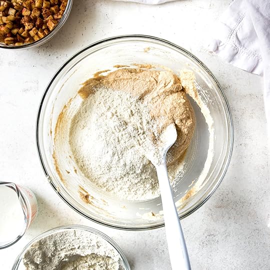 Alternating adding flour and buttermilk to apple muffin batter, in a glass bowl with a light blue spatula. 