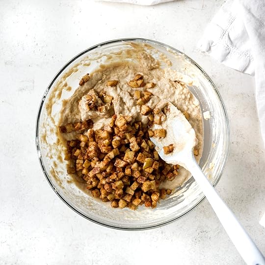 Finely diced apples covered in brown sugar and spices are folded into muffin batter with a silicone spatula.