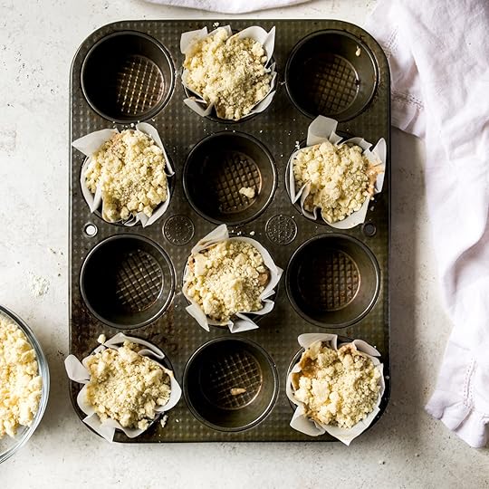 Blonde streusel on top of apple muffin batter in a muffin pan just before going into the oven to bake.