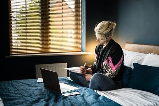A woman sitting on her bed with an open laptop before her, writing in a journal. You are your life’s protagonist.