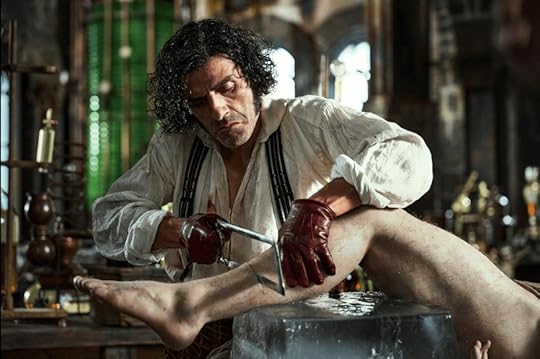 Victor Frankenstein, played by Oscar Isaac, in a white shirt and red gloves, sawing into a limb in his lab.