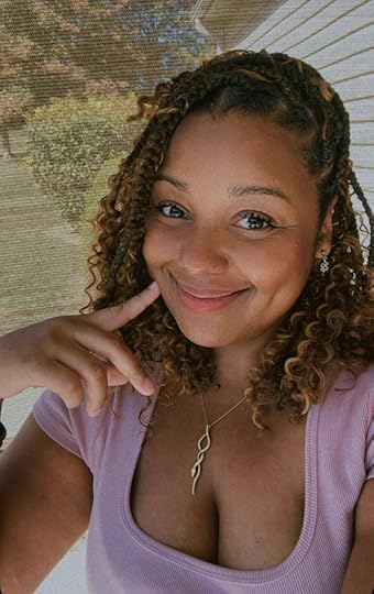 Headshot of the author, a smiling Black woman with a light purple top and silver pendant necklace, and shoulder length curls.