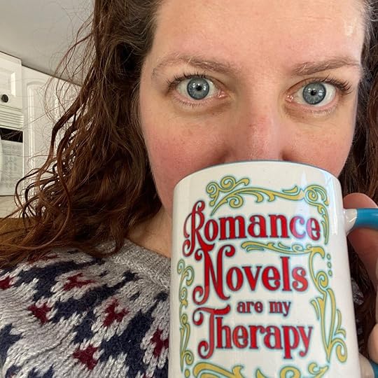 A selfie of a woman with red hair and blue eyes sipping a mug that says 