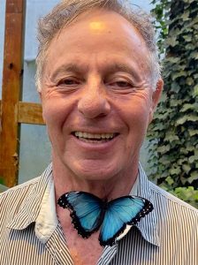 A picture of Shya's smiling as a blue morpho butterfly rests on his neck.