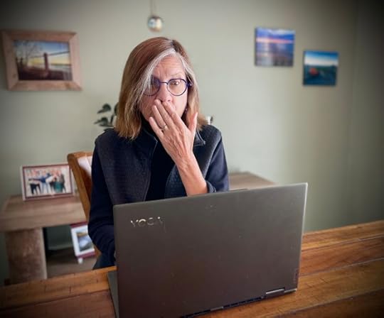 A woman sitting at a desk, looking surprised and covering her mouth with her hand while using a laptop.
