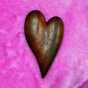 A wooden heart on top of a pink velvet background.