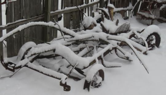 The chassis of a Model A Ford covered in snow, it is next to a dilapidated fence, and disused ferret cage is also present.
