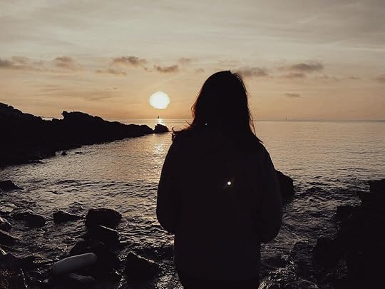 a woman standing on a rocky beach watching the sun set