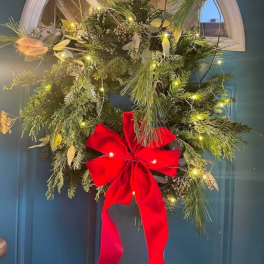 Evergreen wreath with red ribbon bow, illuminated by mini LED lights against blue background