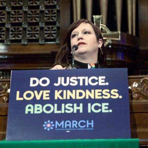 Rev. Ashley Horan at pulpit with a sign on it that says 