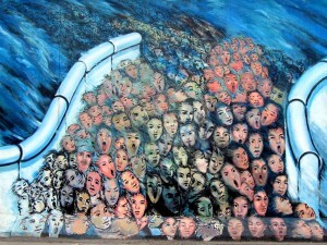 A section of the Berlin wall with faces of many people crowded together and crying out