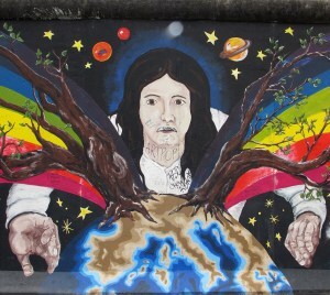 A section of the Berlin Wall depicting a woman embracing the earth, flanked by a rainbow and crowned by the planets