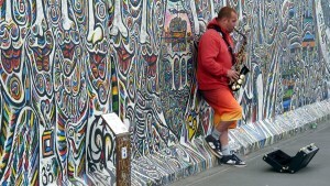 Man playing the saxophone while leaning against the Berlin Wall
