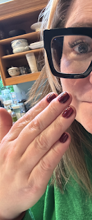 A woman (me!) partially pictured at the side of the shot, holding up her hand to show deep burgundy nail varnish.