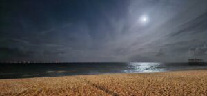A shingle beach and the sea under moonlight.