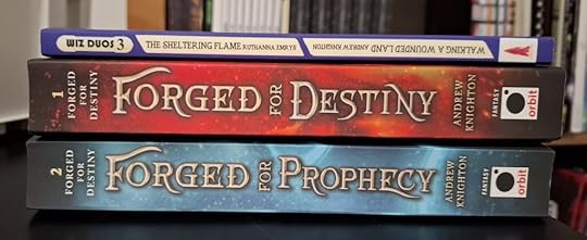 The books in a stack, spines out: Wiz Duos 3, containing The Sheltering Flame by Ruthanna Emrys and Walking a Wounded Land by Andrew Knighton: Forged for Destiny by Andrew Knighton; and Forged for Prophecy by Andrew Knighton.