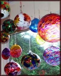 This may contain: colorful glass ornaments hanging from the ceiling in front of a window, with trees outside