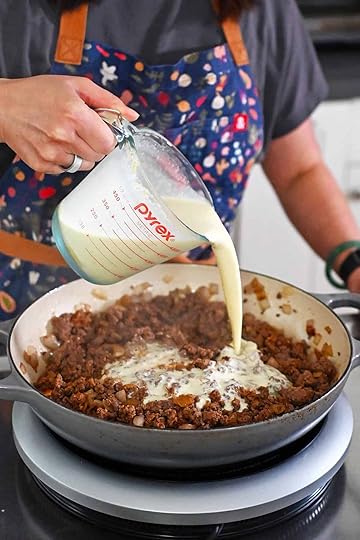 Pouring the dairy-free sauce into a large skillet filled with cooked and seasoned ground beef and diced onions.