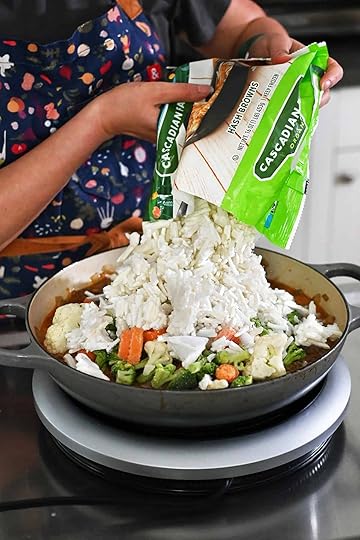 Adding an open package of frozen hash browns into the skillet with seasoned ground beef, diced onions, dairy-free sauce, and mixed frozen vegetables.