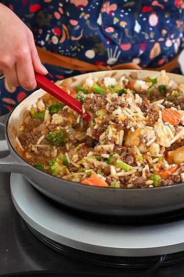 Mixing the contents of the skillet well with a red silicone spatula to integrate the frozen vegetables with the sauce and beef.