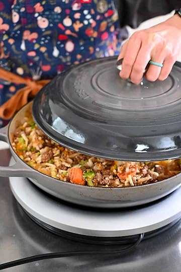 Placing a lid on top of a skillet filled with ground beef, potatoes, and frozen vegetables so it can cook evenly.