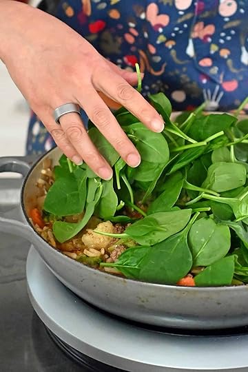 Adding fresh baby spinach to a skillet filled with cooked ground beef, potatoes, and mixed vegetables.