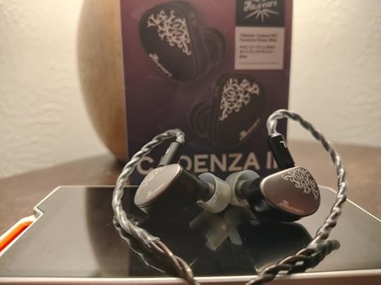 Photo of two earbuds on top of a portable device, with a box in the background.