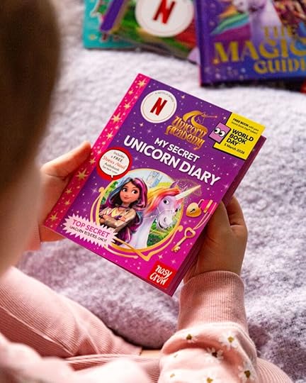 A child is holding a copy of the book, My Secret Unicorn Diary, from the TV-Tie in Series, Unicorn Academy.