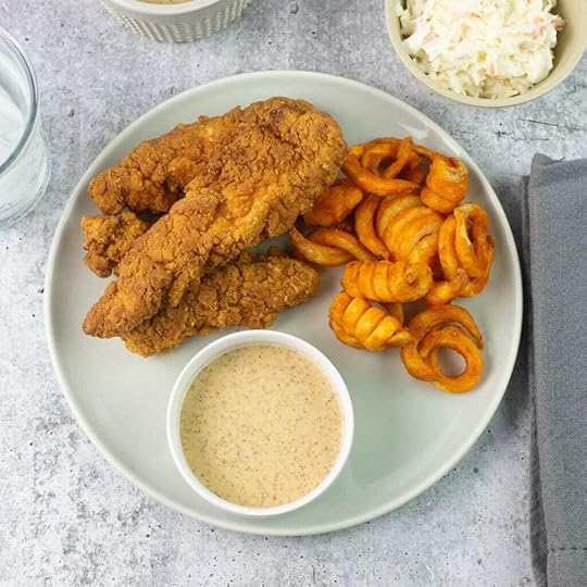 Bowl of honey mustard dipping sauce on plate with tenders and fries.