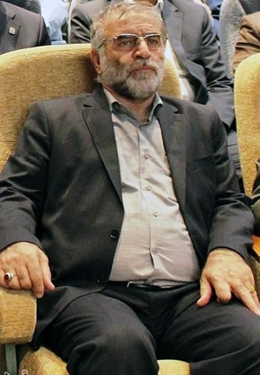 A middle-aged man with a beard and glasses sitting in a chair, wearing a dark suit and light shirt, with an expression of contemplation.