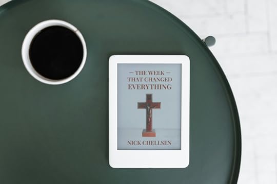 An e-reader resting on a round green table next to a cup of coffee, displaying the book cover The Week That Changed Everything by Nick Chellsen, featuring a wooden cross at the center.