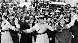 Crowd of people gathered around officers in uniform, holding hands to create a barrier, set in a historical context.