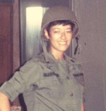 A woman wearing a military uniform and a helmet, smiling and posing indoors.