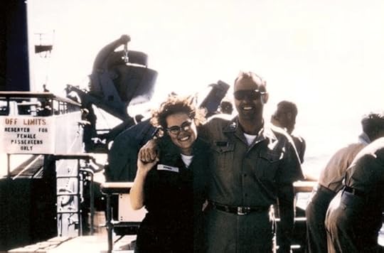 A smiling woman in military attire poses with a man in uniform on a ship's deck, with a sign in the background indicating off-limits areas.
