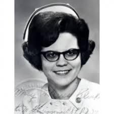 A black and white portrait of a smiling woman wearing glasses and a nursing cap, dressed in a nurse's uniform.