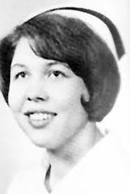 Black and white portrait of a young woman wearing a nurse's uniform and cap, smiling at the camera.