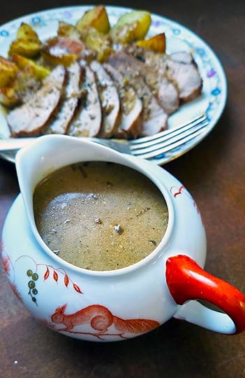 A gravy boat with sour cream gravy in front of a plate of pork sauced with the gravy.