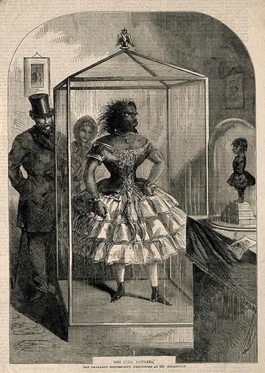 An illustration of a woman named Miss Julia Pastrana, known for her unusual appearance, displayed in a glass enclosure, wearing a frilly dress. A man in a top hat and a woman are observing her. The setting suggests a 19th-century exhibition.
