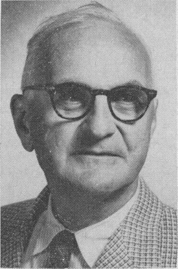 Black and white portrait of an older man wearing glasses and a checkered suit.