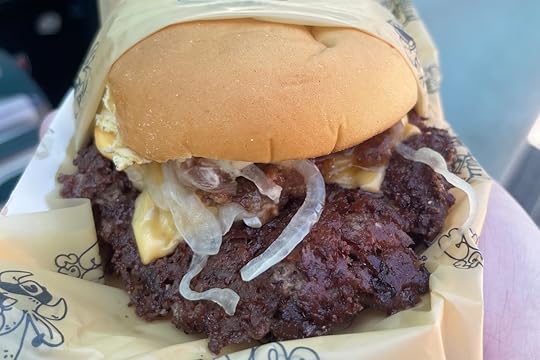 Close-up of Cowy Burger smash burger with American cheese, grilled onions, bacon jam, and sauce on a potato roll