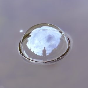 Bubble on the surface of water reflecting the sky and silhouette of a person