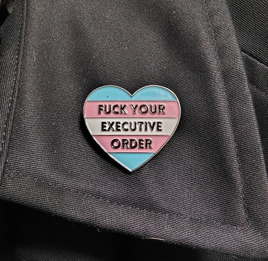 a heart-shaped pin with trans-flag colors that says, 
