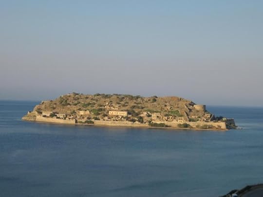 A scenic view of a desolate island with ruins and greenery, surrounded by calm blue waters under a clear sky.