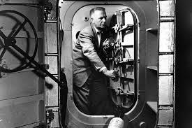 A man in a suit standing in the doorway of a large safe, adjusting the locking mechanism.