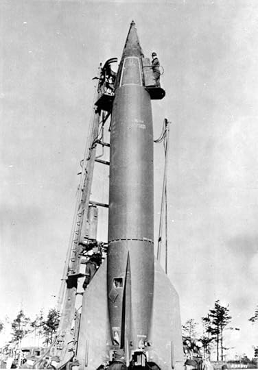 A black and white image of a large missile being prepared for launch, with technicians working on it and a wooden ladder leaning against the structure.