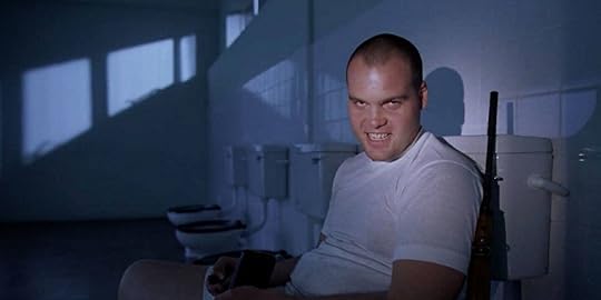 Vincent D'Onofrio sneers while sitting on a toilet, next to a rifle, in 
