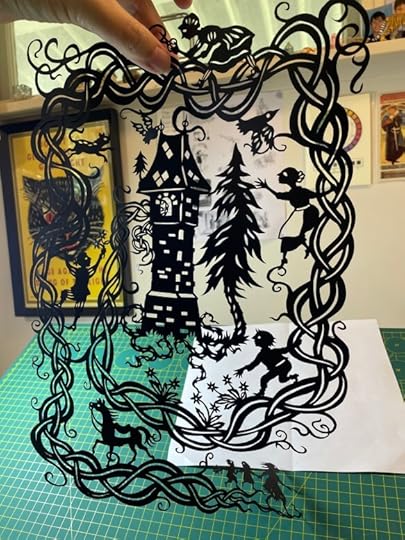 Hand holding a cut-paper silhouette of the story of Rapunzel following a braid emerging in a spiral from a tower