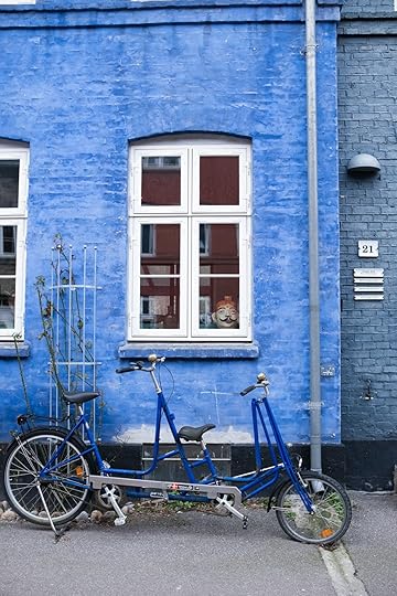 A blue tandem bicycle is parked against a blue building.